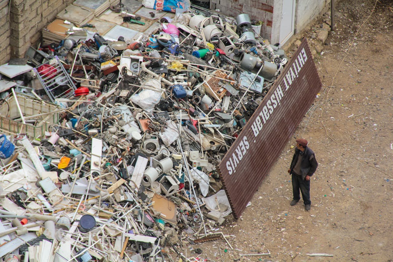 brand-01 A person inspecting a large pile of scrap metal and electronic waste in an outdoor junkyard.